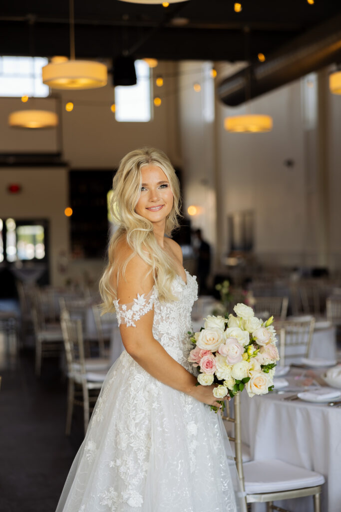 bride standing in the District Venue Ankeny in her wedding dress holding her wedding flowers smiling softly at the camera