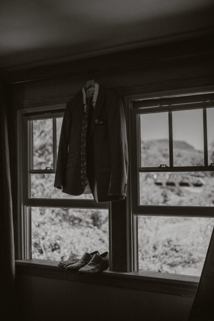 A tuxedo jacket hangs up next to a window.