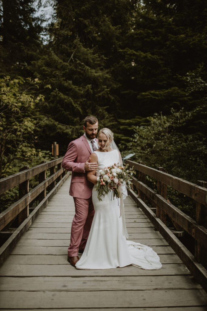 A just-married couple poses in a forested area on a bridge.